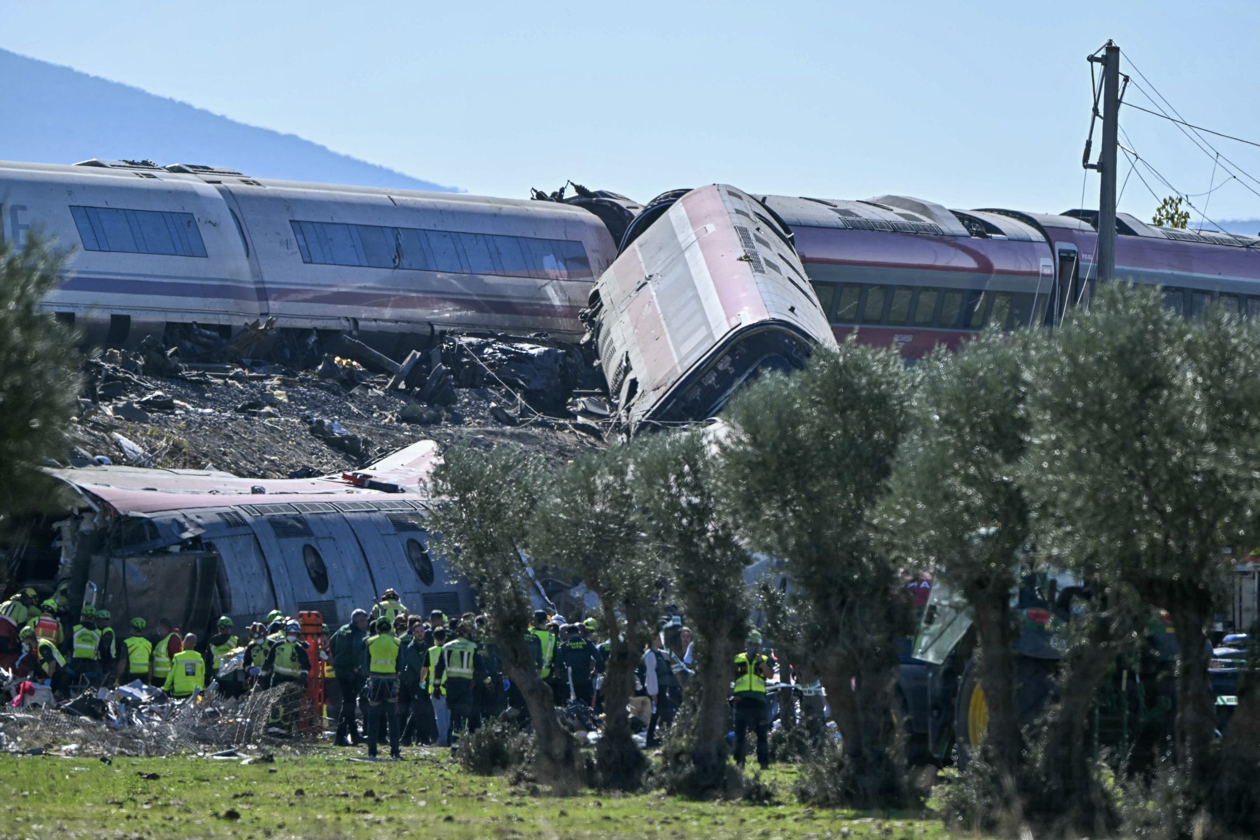 Rescue workers at the scene of a train collision in central Spain, amidst debris and emergency vehicles.